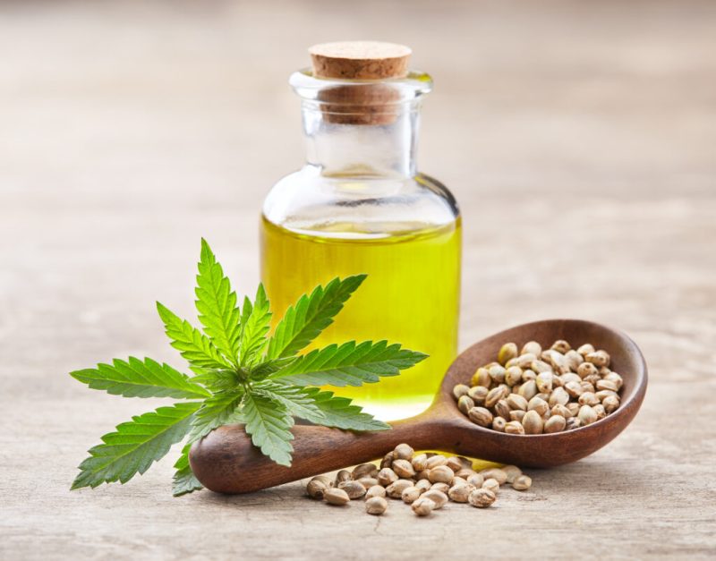 Hemp oil with seeds and cannabis plant on wooden board